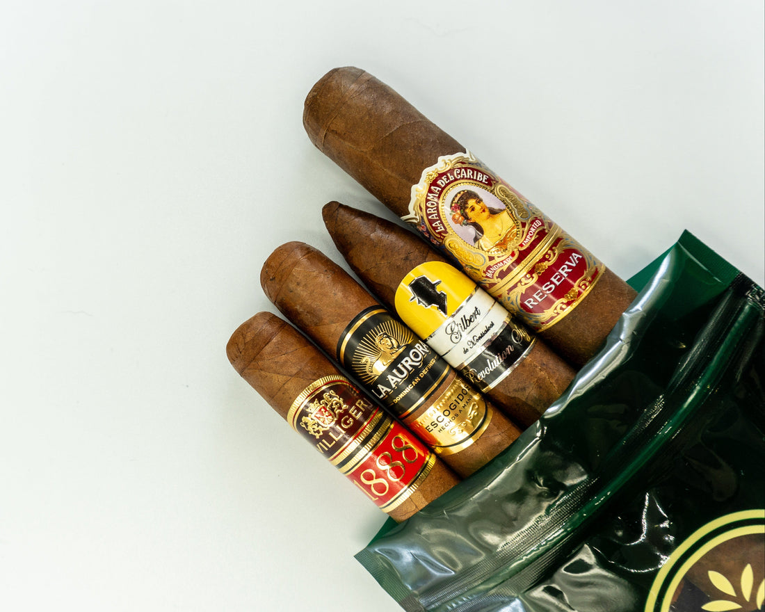 Four premium heritage cigars — Gilbert de Montsalvat, La Aroma del Caribe Reserva, La Aurora Escogidos, Villiger 1888 — on The Gentlemen's Cigar Pack signature packaging, Switzerland.