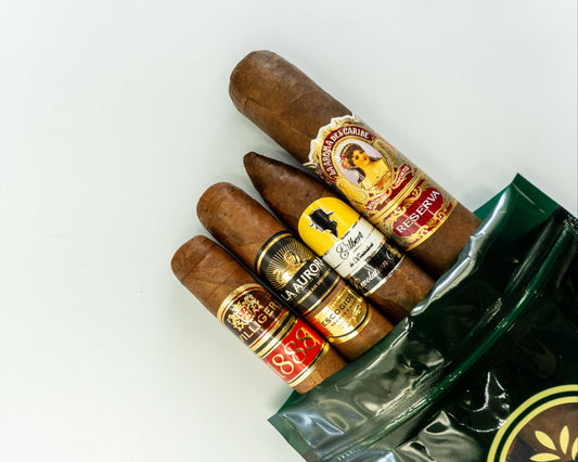 Four premium heritage cigars — Gilbert de Montsalvat, La Aroma del Caribe Reserva, La Aurora Escogidos, Villiger 1888 — on The Gentlemen's Cigar Pack signature packaging, Switzerland.