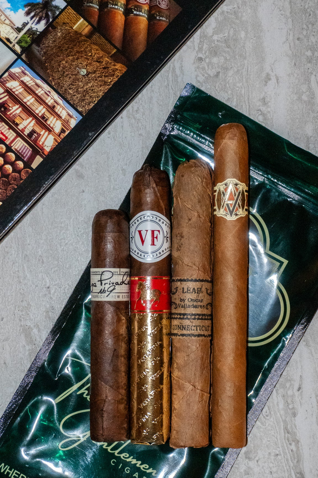 Four premium cigars - Leaf by Oscar Connecticut, AVO XO Maestoso, VegaFina Year of the Horse 2026, Drew Estate Liga Privada No. 9 — displayed on The Gentlemen's Cigar Pack signature packaging, Switzerland.